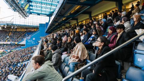 A photo of football fans and some of the Brown Girl Sport community watching Chelsea v Arsenal at Stamford Bridge in the Women's Super League