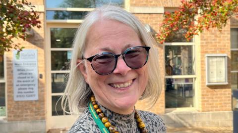 Picture of Christine Wise. She has white shoulder length hair and is wearing dark glasses.