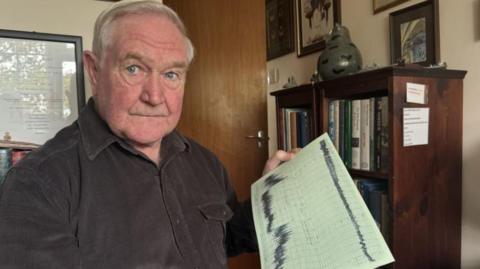 Pete Legg in  a dark shirt holding the anemograph wind reading from the Great Storm in 1987