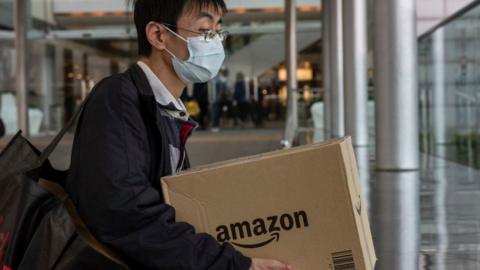 A man wearing a surgical mask carries an Amazon delivery box in Hong Kong