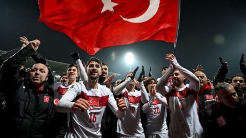 Turkey players celebrate reaching the World Cup in front of Turkey flag