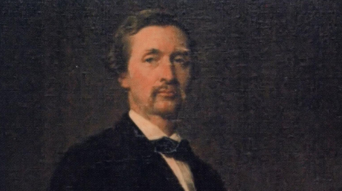 Portait of a young Lord Henry Stanley, who has short fair hair and moustache. He wears a tie or cravat with his suit. It is on a black background.