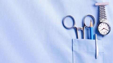 A pencil, pen, scissors and a watch on a nurse's uniform