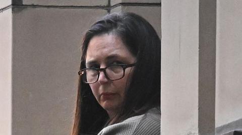 Erin Patterson, with long brown hair and wearing dark glasses, is looking over her left shoulder to the right