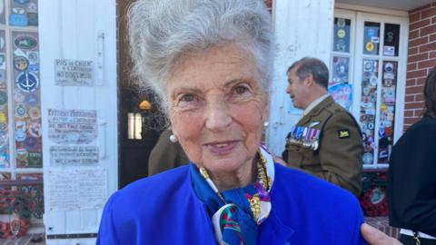 Arlette Gondree outside a café wearing a blue suit and wearing pearl earrings