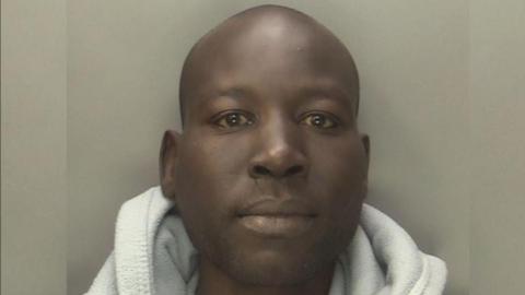Mohammed Abdulraziq is pictured with a blank expression, wearing a grey shirt underneath a grey hoodie. He is against a grey background.

