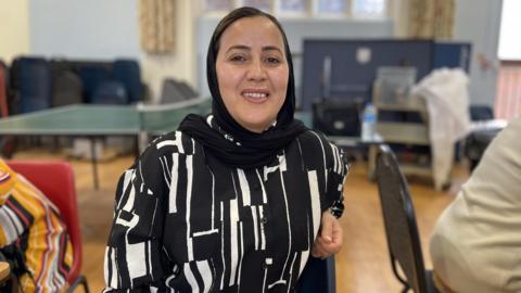 Zarifa, a women sitting on a chair looking at the camera, wearing a black and white outside, and smiling