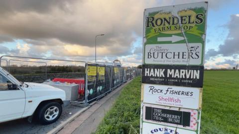 A sign to the right and roadworks to the left. The sign is on a grassy area, and the roadworks are fenced off.