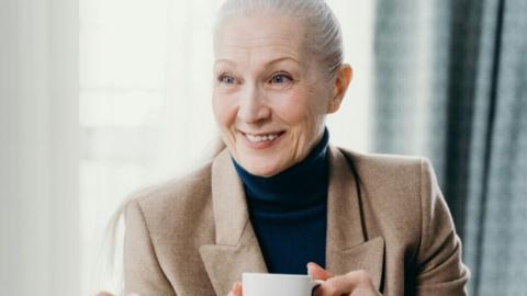 Lady with grey hair smiling, holding a cup of tea