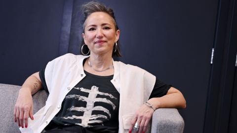 KT Tunstall, wearing a black t-shirt, white cardigan and sitting on a grey sofa