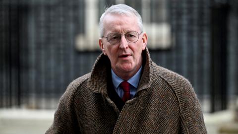 Hilary Benn on Downing Street wearing a brown coat over and suit and tie