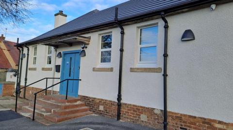Vogrie Hall is a single-storey building with four windows along its white, harled exterior wall and a blue front door.