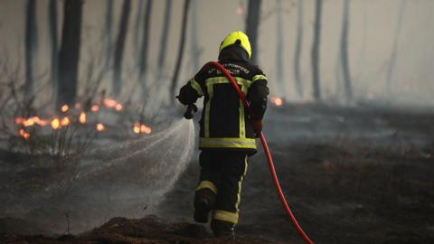 A firefighter carrying a hose spraying water on a fire