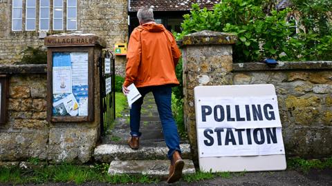 A person in an orange anorak enters a polling station at a church in Walditch on 2 May