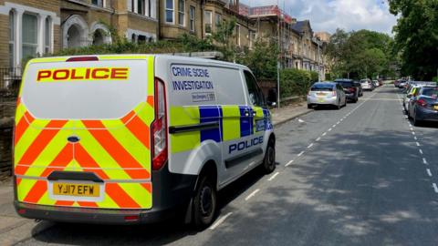 A Crime Scene Investigation police van parked on a street of terrace houses.
