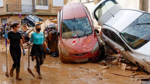 Two people wearing face masks and carrying a spade and brush walk down a muddy flood-hit street in Catarroja, Valencia province, with damaged cars stacked alongside each other on the side of the street. Picture date 5 November.