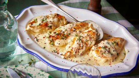 A white dish full of four chicken breasts in a creamy sauce.