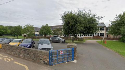 The front of Glendale school in Wooler with cars in the carpark and the school behind 