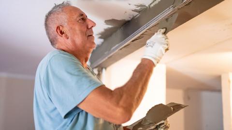 An older man plastering a ceiling