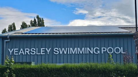 The exterior of Yearsley Swimming Pool in York. The roof of the structure is covered in solar panels and the side of the building bears the pool's name in white letters.