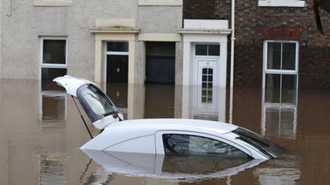 White car mostly submerged in flood water on a residential street