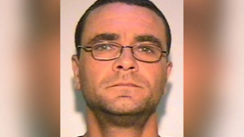 Andrew Malkinson is photographed with short brown hair, glasses and light stubble. The image was issued by police after his arrest in 2003.
