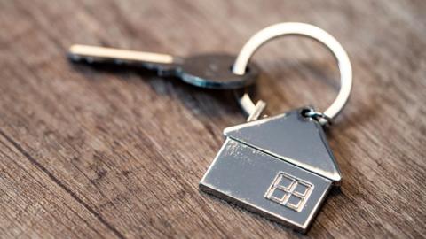 A house key attached to a house shaped fob lying on a dark wooden table.