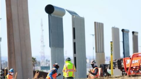 Construction workers build a secondary border wall with the prototype models in back, on February 22, 2019 in Otay Mesa, California