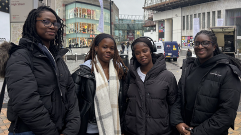 Four women standing outside the Bullring Shopping centre wearing coats. They are all looking into the camera.