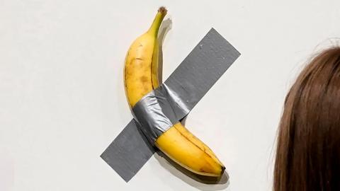 A banana taped to a white wall with grey tape