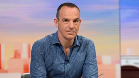 Martin Lewis wearing a blue shirt in front of a blue and orange background