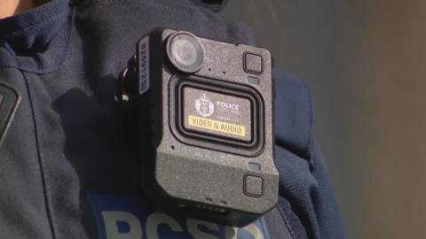 A close-up shot of a body-worn camera on a police officer's chest. It is a black rectangle that reads "Police Scotland Video & Audio".