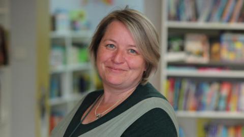 Leanne Fridd, who has brown, shoulder-length hair, smiles as she stands in her bookshop