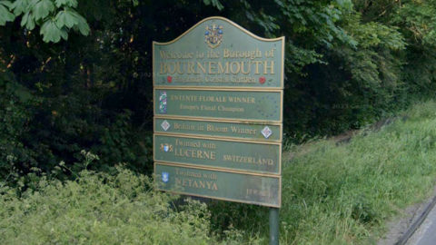 A green sign on the side of the road which reads "welcome to Bournemouth" and further down the sign reads "Twinned with Lucerne, Switzerland" and "Twinned with Netanya, Israel".