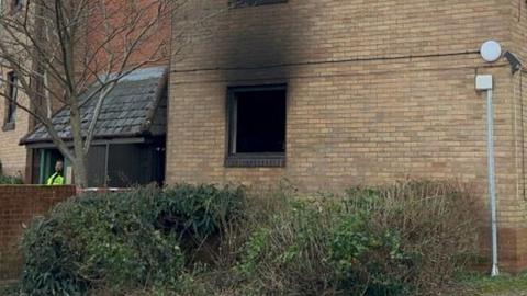 Smoke damage to the flat building's brick wall above a ground floor window.