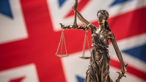 The statue of justice, goddess of justice in front of UK flag