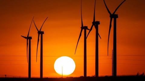 A Texas wind farm BP later sold, with turbines seen in silhouette against a red sky and setting sun 