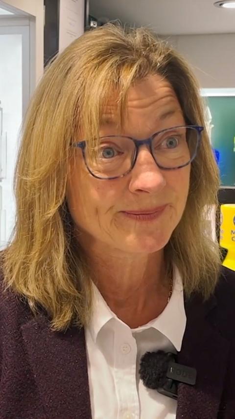 A woman with blonde hair wearing blue glasses and a claret suit.