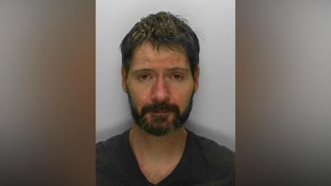 A mugshot of a man with short hair and a beard, facing the camera.
