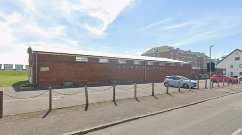 A single story brick building with only small windows near the roof. The words "swimming pool" are written on the side of the building in an outdated font.