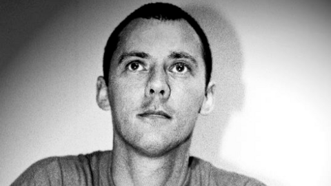 A black and white photograph of a man, shoulders and head in view, looking ahead. He has a buzz cut and what appears to be a grey top on.