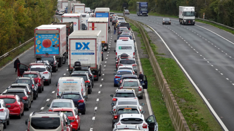 Stock image of cars in standstill traffic on a motorway. Some drivers have opened their car doors to get out and are standing in the three lanes of traffic. 