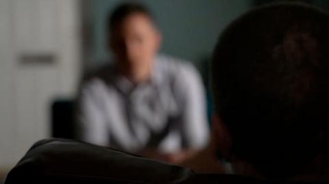 Blackout of interviewee with fuzzy shot of BBC journalist in the background.