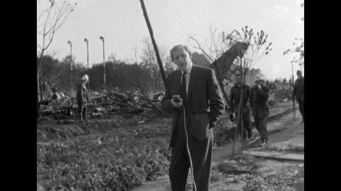 Reporter Peter Woods standing in front of the wreckage, with firemen behind him.