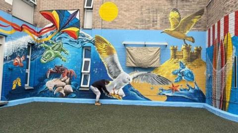A mural including a bird and fish in the middle. It is on a blue background.