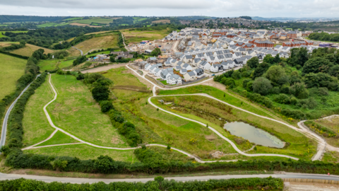 An aerial view of Sherford new town, with houses to the right and green space and paths to the foreground and left. 