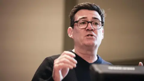 Andy Burnham speaking at an event, he is wearing a dark jumper