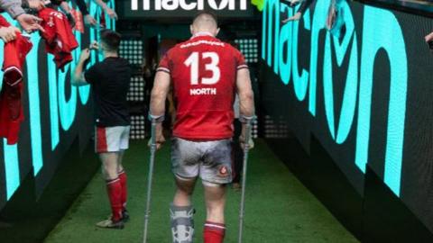 Rear view of George North walking on crutches