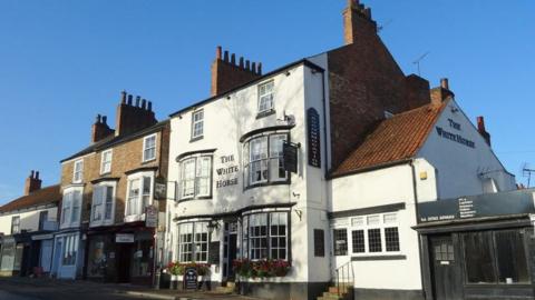 The White Horse pub in Ripon. A three-story building painted white at the front with black bow windows either side of a main entrance.