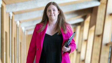 Gillian Mackay wearing a pink blazer over a black shirt as she walks through a corridor in the Scottish Parliament 